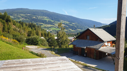 Fototapeta na wymiar Panoramablick von einem erhöhten Punkt über die bergige Landschaft mit wolkenreichem Himmel. Im Vordergrund kleine Holzhäuser