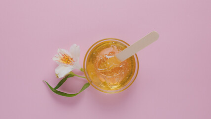 Liquid yellow sugar paste, wooden spatula and flower on a pink background. Removing unwanted hair. Sugaring.Depilation. Epilation. Beauty.Place for text. - obrazy, fototapety, plakaty
