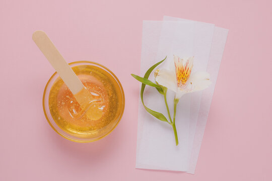 Liquid yellow sugar paste, wooden spatula, flower and depilatory strips on a pink background. Removing unwanted hair. Sugaring.Depilation. Epilation. Beauty.