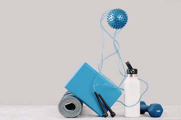 Rolled blue yoga mat. Yoga block weighing scale dumbbell water bottle on grey. Gender neutral fitness and exercise concept. Levitating massage ball. Active lifestyle sport. Workout at home or gym