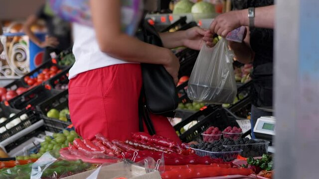 A Customer Buys Fresh Fruit from the Market with Cash. Sale of fruits on open counters, shelves. Retail trade of seasonal fruits. Ripe berries, grapes, churchkhela are lying on the counter. Zoom.