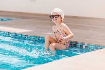 Cute toddler girl wear swimsuite having fun in pool with blue clean water. Family vacation in luxury resort