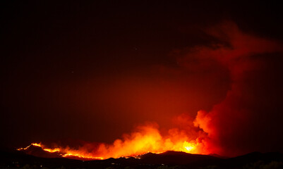 Wildfire engulfs small mountain area next to community.  Billowing smoke clouds fill the air