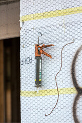 Caulk gun hanging on a wall covered in metal construction mesh