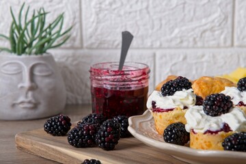 Scones with homemade blackberry jam, cream and fresh blackberries, with jar of jam and spoon on wooden board