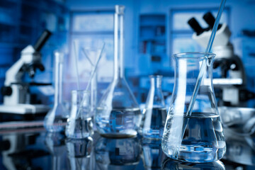 Laboratory investigations concerning test and medicine against covid. Microscope, glass tubes and beakers on blue background.