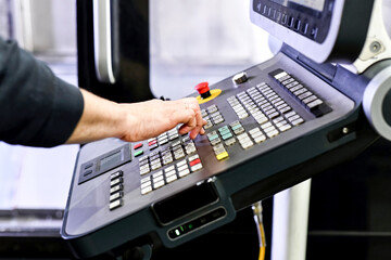 The man uses the remote control from the CNC machine.