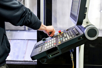 With the help of the control panel from the CNC machine, a man makes blanks.