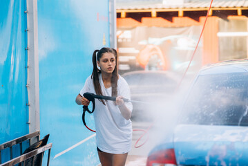 Brunette from a high-pressure hose washes the car at a car wash