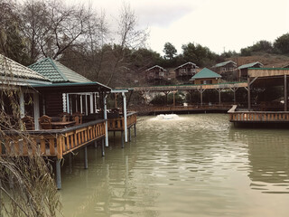 Fototapeta premium Street cafe with simple wooden interior on the shore of a picturesque lake. Authentic cafe with wooden tables and chairs near the Achigvar lake. Part of the terrace of the summer restaurant behind a w