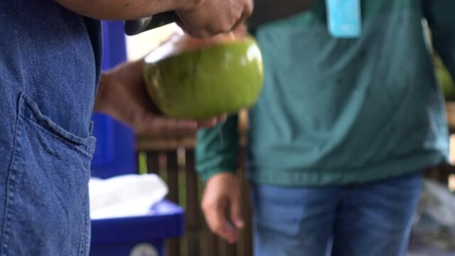 Hand with knife manually cut open green fresh coconut for juice
