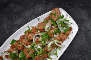 LULYA-KEBAB with herbs and onions on a plate, on a dark background
