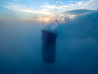 High chimney of a thermal power plant above the fog in the rays of the sunset. Aerial drone view.