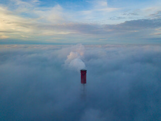 High chimney of a thermal power plant above the fog in the rays of the sunset. Aerial drone view.