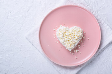 Heart shaped cottage cheese in a pink plate on a white table. Copy space for text