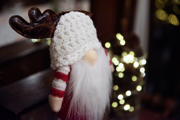 Fototapeta Ozdoba świąteczna, skrzat w ciepłej czapce, z białą brodą i porożem renifera. W tle światełka choinkowe obraz