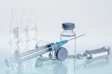 syringe and diferent kind of ampoules and vials close-up on white background with reflection