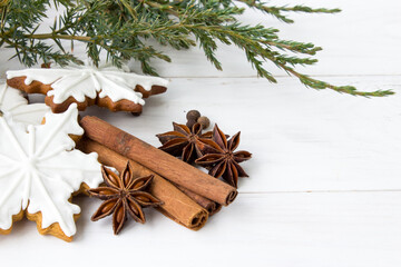 Gingerbread cookies in white glaze, cinnamon, spices and juniper branches on a light wooden background. Christmas gingerbread. Edible Christmas decor concept. Christmas traditions. Copy space. Flat la - 475905506