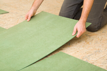 Young adult man hands laying green natural wood fiber insulation board. Preparing surface from fibreboard underlay for laminate or parquet floor. Repair work of home. Renovation process. Closeup.