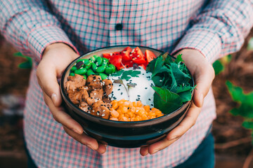 a man holds a poke bowl with chicken and sauce