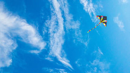 Kite blue sky. Colorful high flying toy. Air kite fly on wind clouds. Rainbow kite in summer background. Concept of dreams, freedom, childhood.