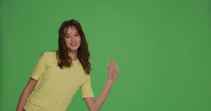 Smiling girl greeting, wave hand say hello or bye to subscribers, peek out on chromakey green background with copy space