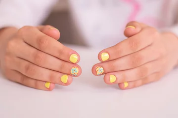 Fototapeten Kleine Mädchenhände mit schönen Manikürnägeln, gelber Gelpolitur, Blumendesign © Galina