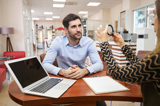 Male listening attentively to optical shop manager with magnifying glass - Powered by Adobe