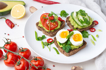 delicious toast with guacamole, avocado, cherry tomatoes, cucumbers, spices, lemon in a white plate on a white background