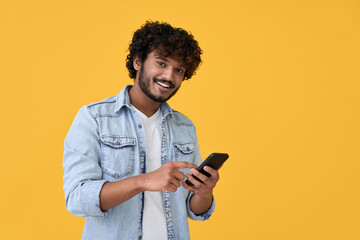 Smiling indian young man using cell phone isolated on yellow background. Happy guy holding smartphone ordering online, making mobile banking payment, advertising application on cellphone. - Powered by Adobe