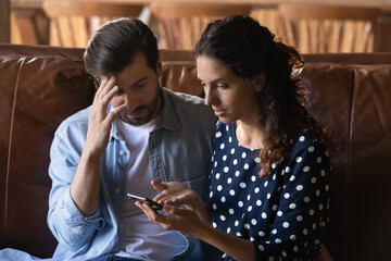 Confused young family couple looking at smartphone screen, feeling stressed of getting message with bad news, bank loan rejection, dissatisfied with broken device or wrong mobile application work.