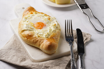 Traditional georgian dish of cheese-filled bread adjarian khachapuri with fried egg on a marble board