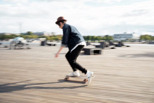 A blurry photo in motion. Milinal is a young man in a hat and a denim jacket. Skateboarding in the city.