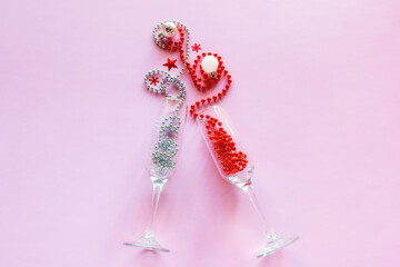 champagne glasses with beads and christmas tree decorations on pink background happy new year christmas