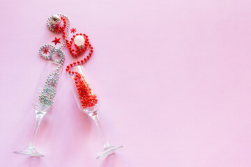 champagne glasses with beads and christmas tree decorations on pink background with place for text happy new year christmas