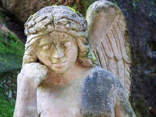 Sculpture of a smilling little angel at forest  tomb cemetery.