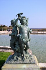 Fototapeta premium Bronze statue of three cherubs on the edge of a basin of the Bassin du Midi in the gardens of Versailles, in front of the west facade of the Palace of Versailles