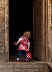 Kleines mädchen steht suchend alleine in türe. Junges Mädchen in rotem Kleid vor dunklem Eingang. Little girl stands alone in door looking. Young girl in red dress in front of a dark entrance.