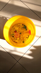 Waste bin with used syringes, vials, test containers, on the tile floor. Hard shadows. Vertical banner. Top View