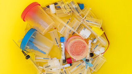 Used syringes, vials, test containers in a yellow bucket. Top View