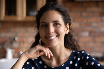 Head shot portrait of latin young female homeowner posing alone indoors in own house. Smiling millennial hispanic woman with perfect skin looking at camera, lady holding distant video call meeting.