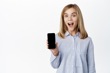 Little girl, teen child showing smartphone screen, mobile phone app display, smiling and looking happy at camera, standing over white background