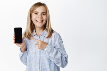 Fototapeta premium Little girl, blond teen child showing empty phone screen, mobile phone interface, video game on application, standing happy against white background
