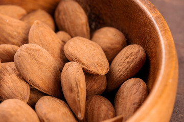 Full wooden bowl of almond nuts on a rustic wooden surface. Dry brown kernels close up