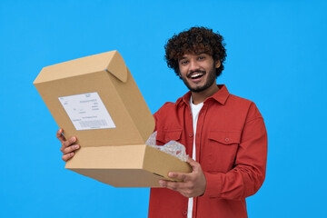 Happy indian young man holding open parcel box isolated on blue background. Smiling guy customer...