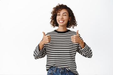 Beautiful cheerful girl showing thumbs up in approval, like gesture, agree, recommending great...