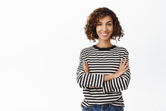Stylish modern middle eastern girl with curly short hair, posing in casual clothes against white backgrund, smiling and looking confident