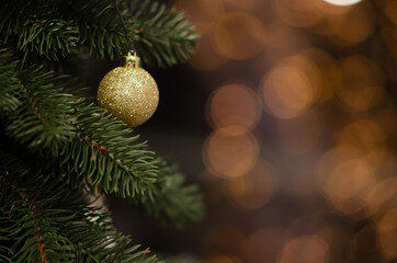 Traditional artificial Christmas tree with gold ball ornament and glowing colorful lights in background with copy space. Soft focus Christmas decorations. Seasonal winter holiday. New year concept.