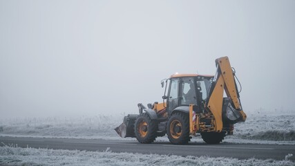 Yellow JCB construction tractor is driving on the foggy road during the cold autumn morning