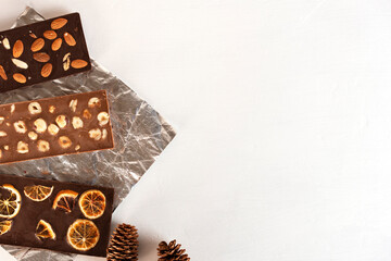 Natural organic milk and bitter chocolate bars with orange slices, almond, hazelnut and fir cones. Copy space.